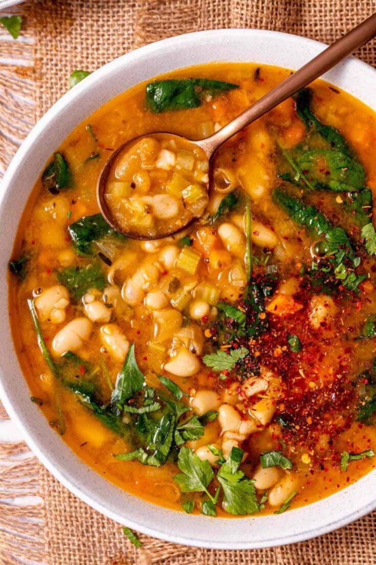 Savory vegetable and white bean soup in a white bowl with chopsticks, topped with herbs and chili flakes, perfect for healthy and comforting meal options.