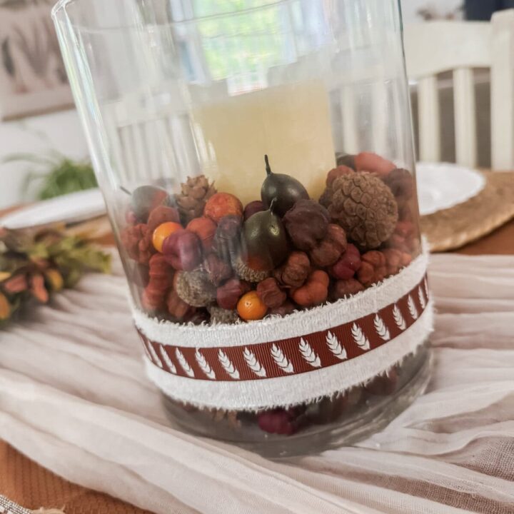 Elegant holiday centerpiece with candles, pinecones, and berries in a clear glass holder.