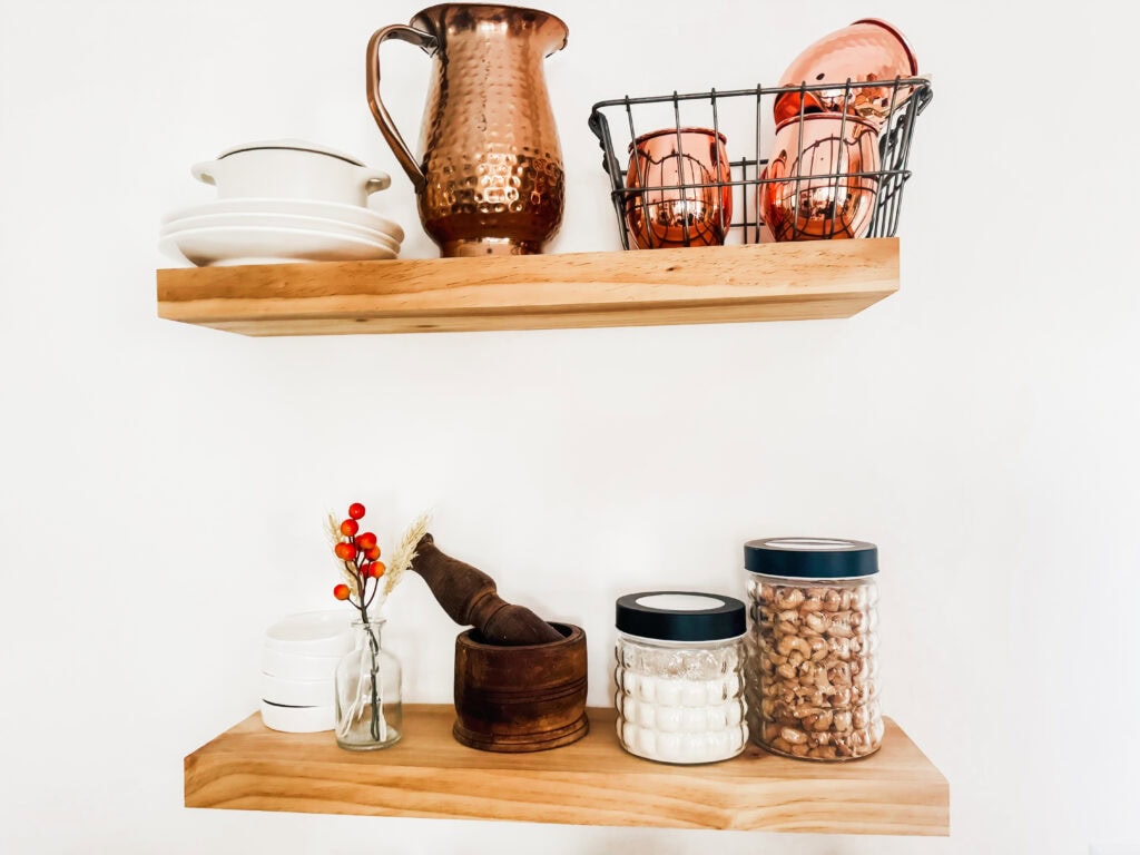 Copper and wooden kitchen decor with jars, dishes, and a mortar and pestle on wooden shelves for a stylish, cozy home aesthetic.
