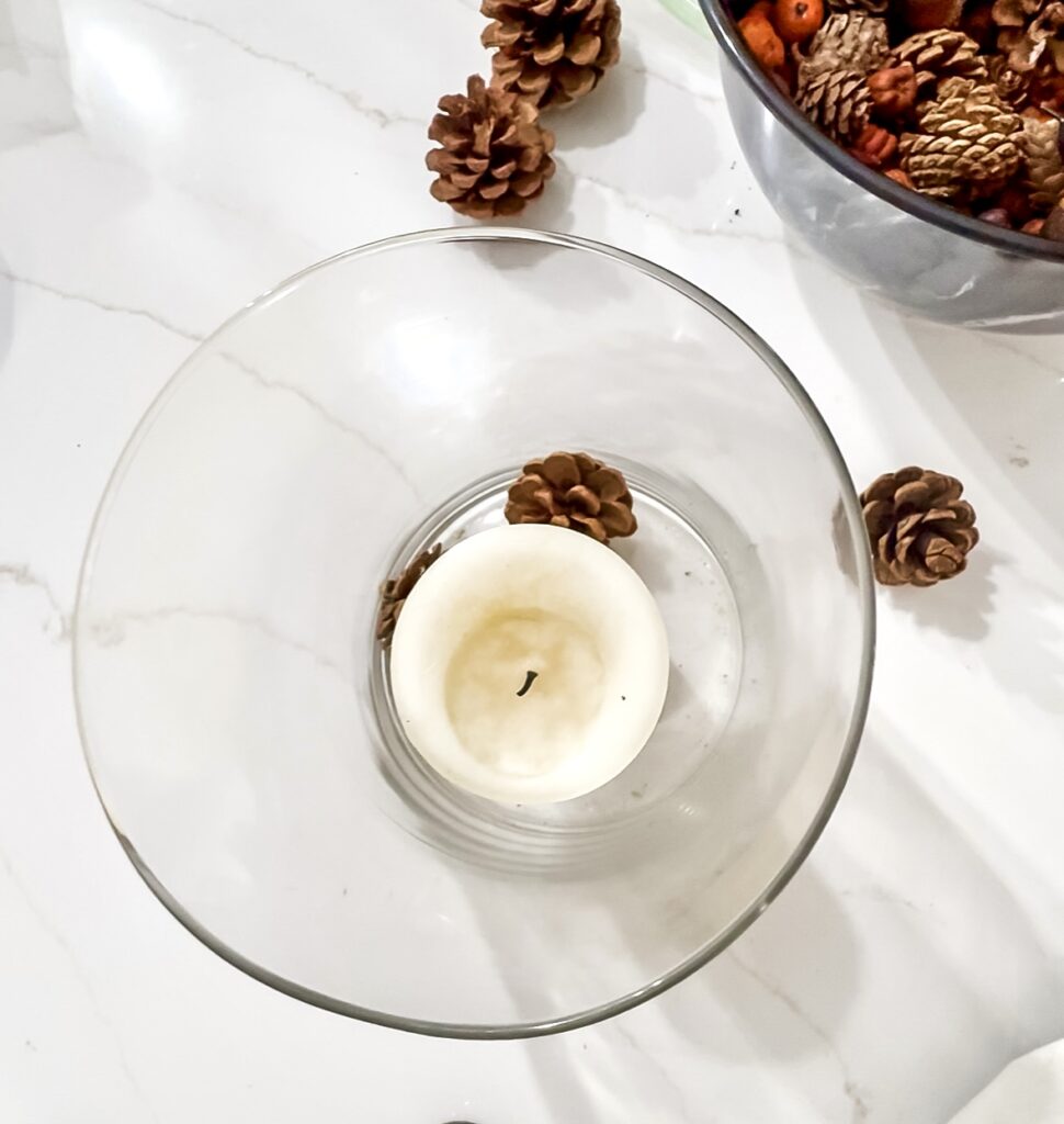 Aesthetic white candle holder with black wick surrounded by pinecones and seasonal decor on a white marble surface for cozy home ambiance.