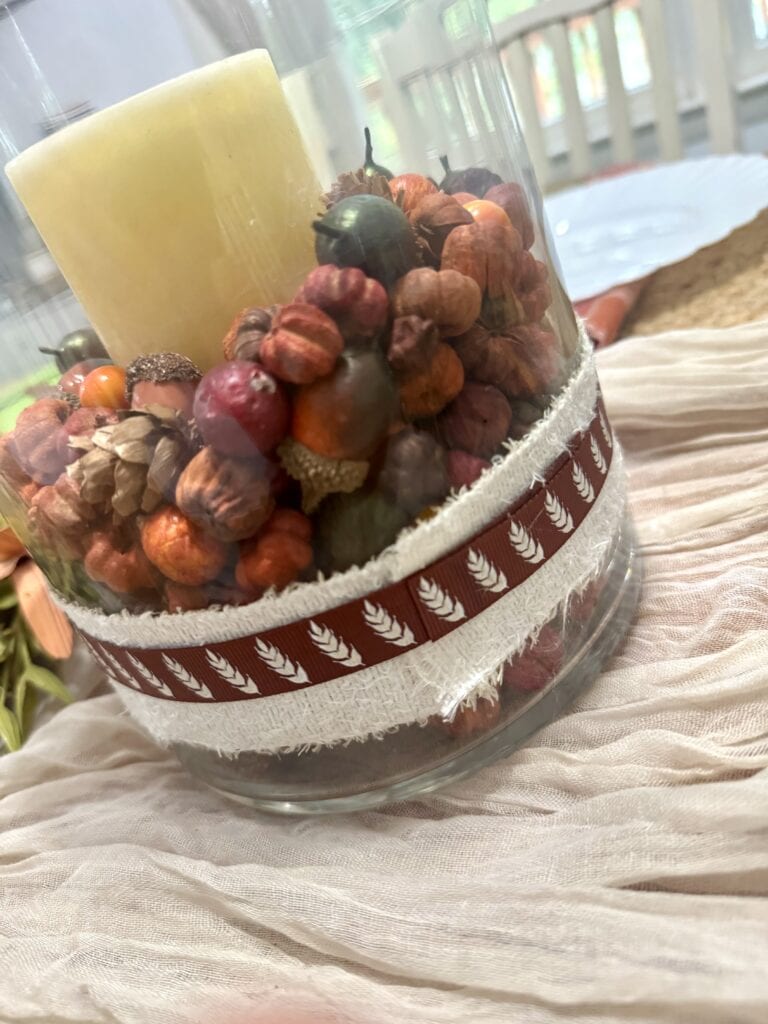 Vase filled with decorated pinecones, a candle, and festive ribbon, perfect for rustic holiday decorations or winter home decor.