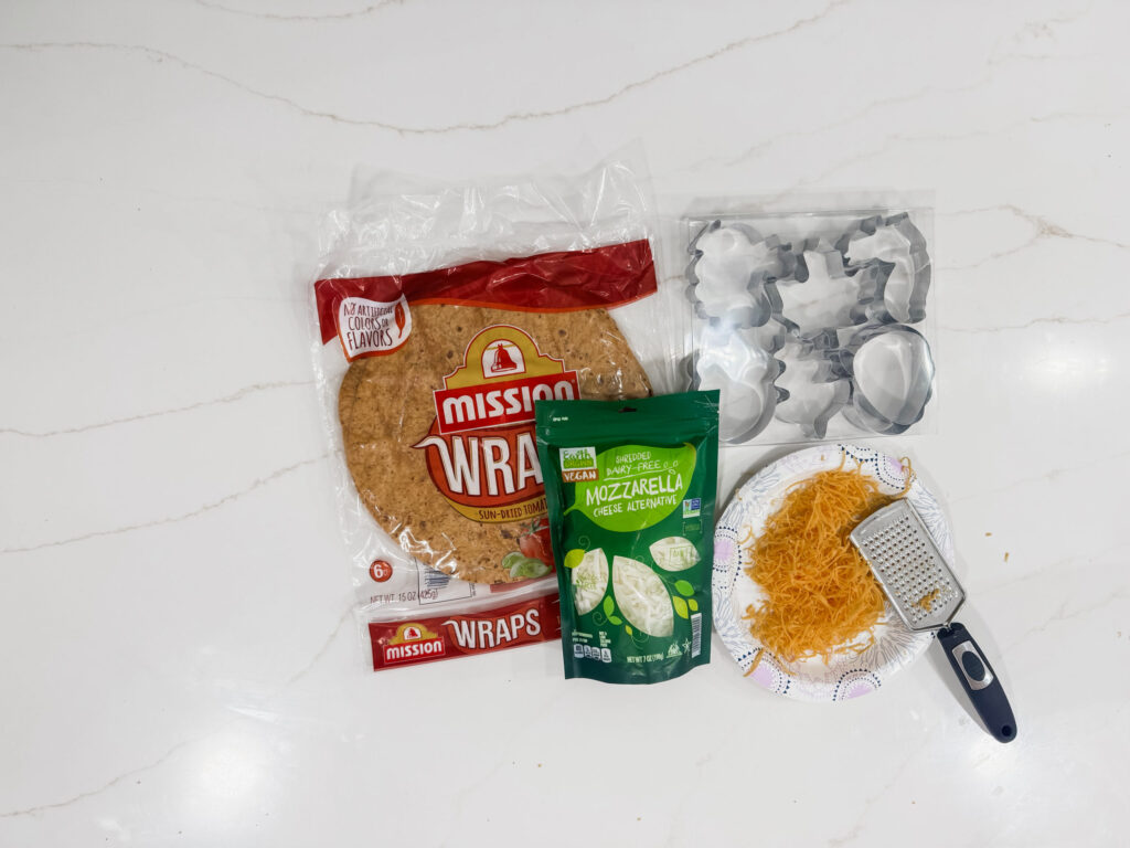 Bright kitchen scene with shredded cheese, cookie cutters, a plant-based burger patty, and a cheese grater on a white marble countertop.