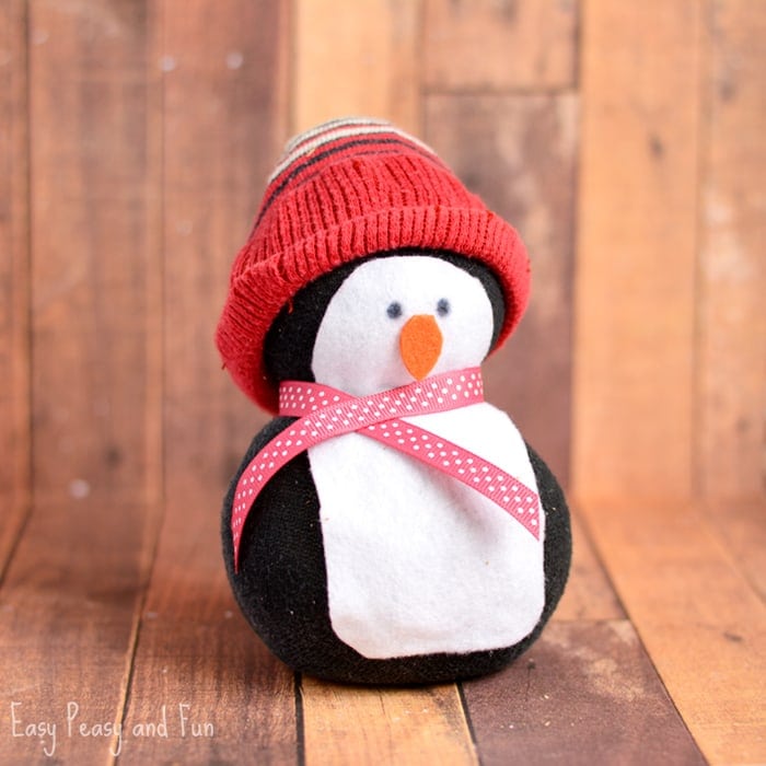 Plush penguin toy wearing a red knit hat and pink polka dot ribbon, adorable winter-themed stuffed animal, perfect for Christmas or cold weather decorations.
