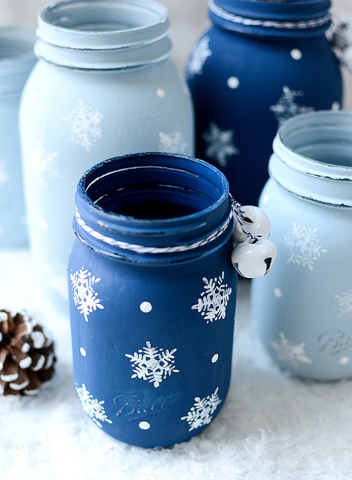 Colorful painted mason jars with snowflake patterns for winter decor and crafts.