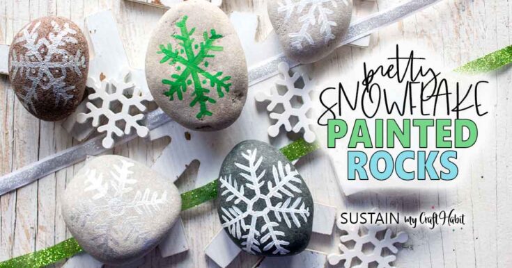 Colorful snowflake painted rocks with white snowflake designs and glitter ribbons, perfect for winter decor and DIY snowflake crafts.