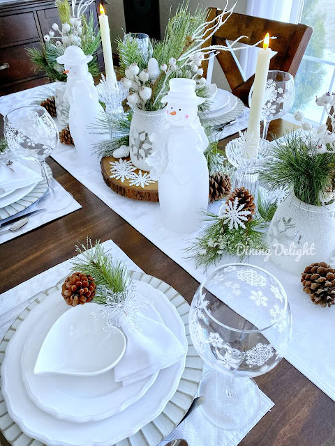 Festive winter holiday table setting with snowman decorations, pinecones, and Christmas greenery for a cozy holiday dinner.