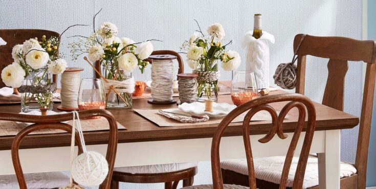 Elegant dining table decorated with white flower centerpieces, knitting yarn, and cozy decor for warm home gatherings.