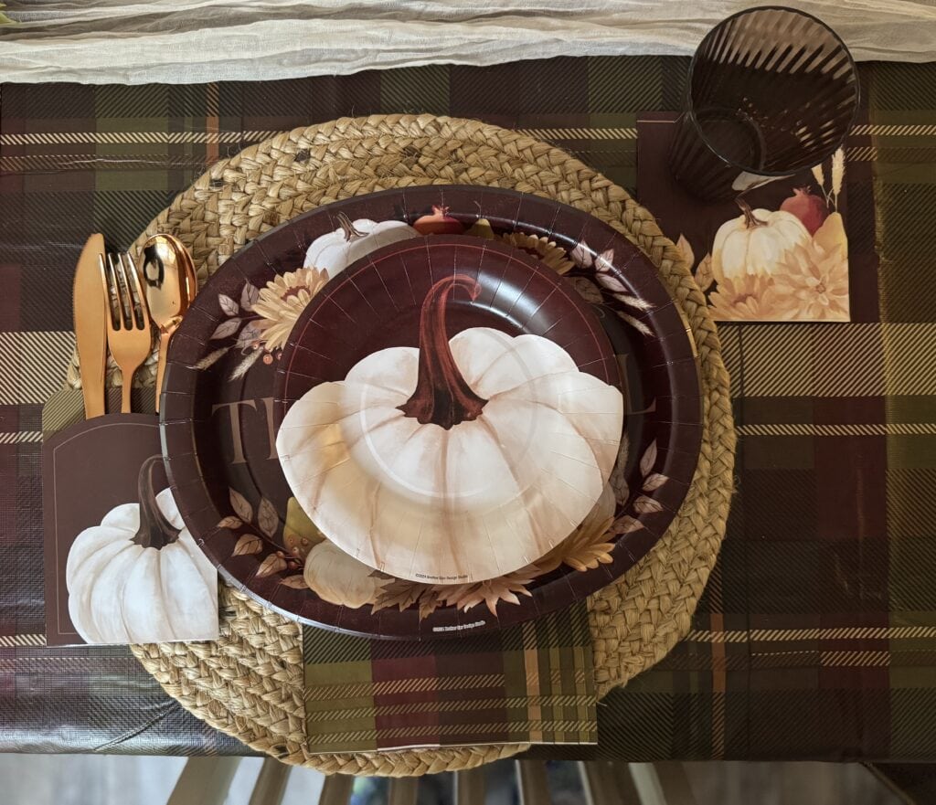 Pumpkin-themed paper plates and autumn decor for fall table setting with plaid tablecloth and placemat.