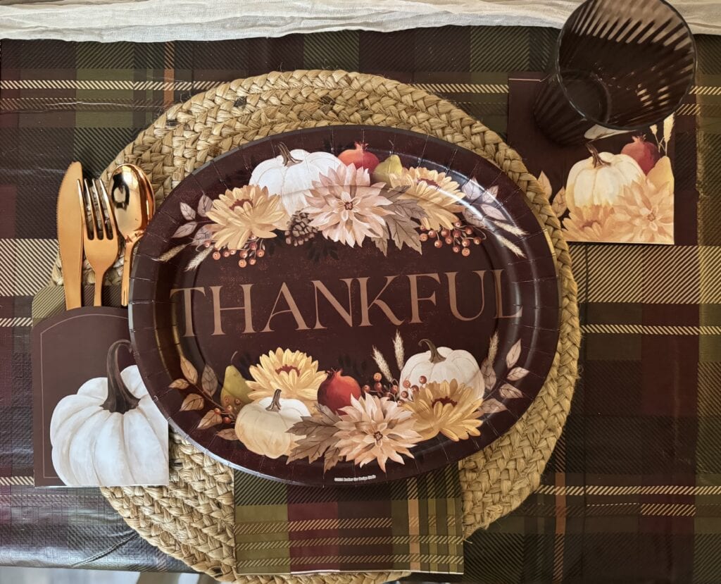 Autumn-themed table setting with a "Thankful" decorative plate, white pumpkins, floral accents, and warm-toned cutlery for fall Thanksgiving celebration.