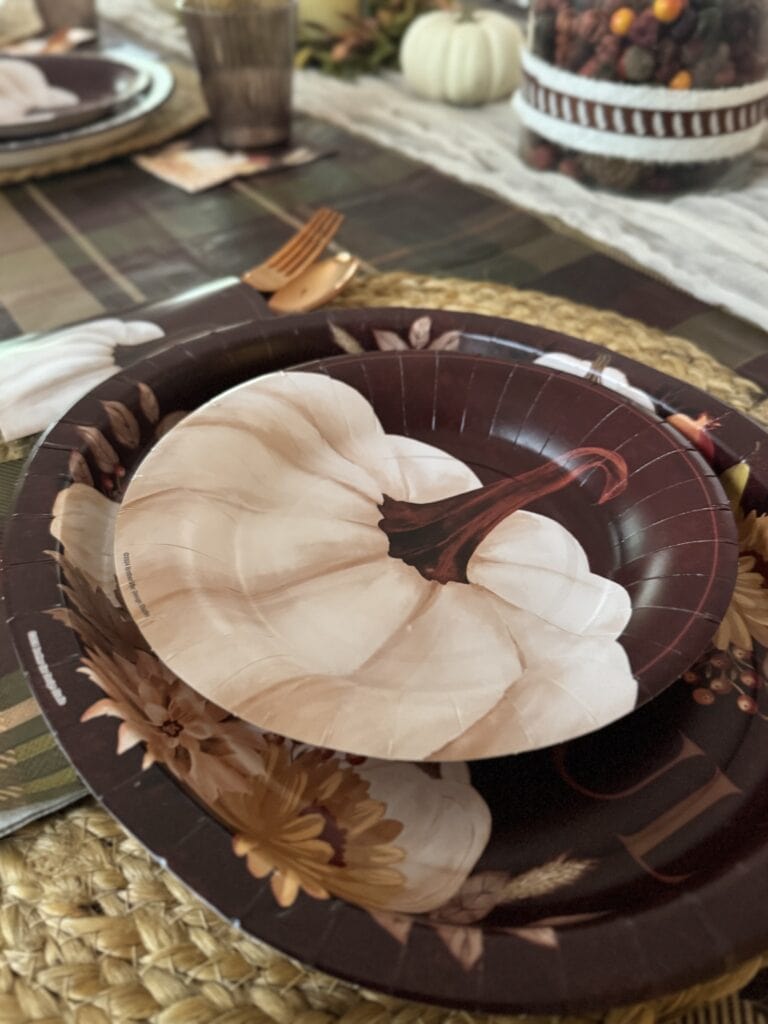 Rustic fall harvest Thanksgiving table setting with pumpkin-themed paper plate, woven placemat, and autumn decor.