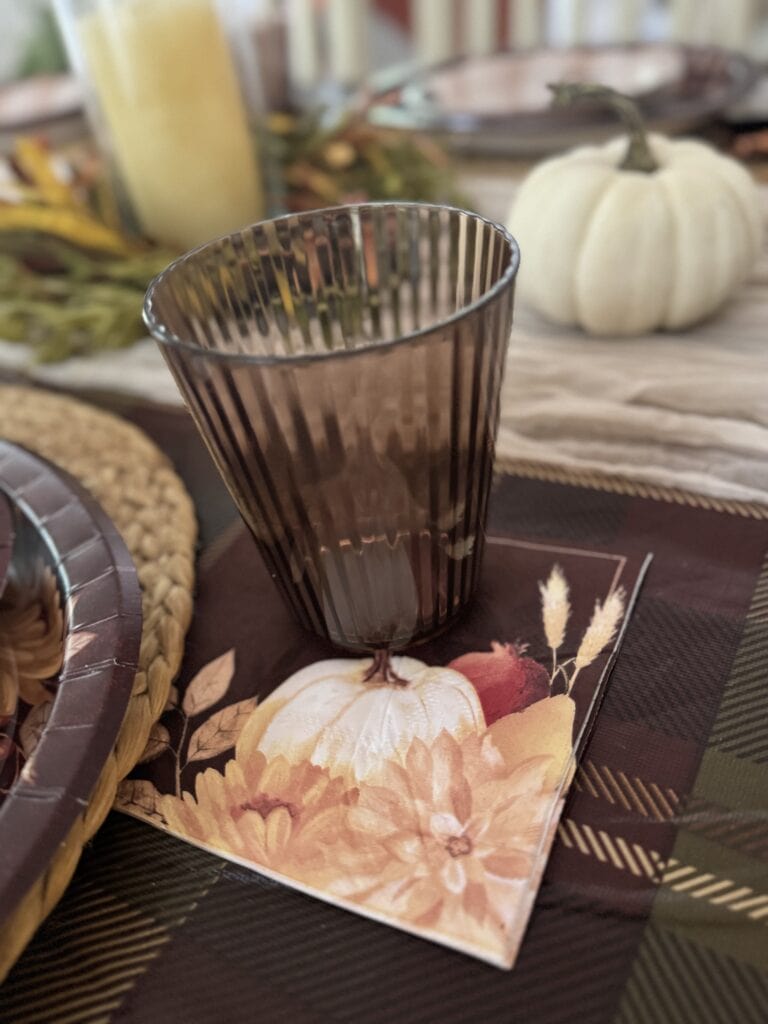 Elegant fall-themed table decor with a brown ribbed glass, white pumpkin, and autumn accents for cozy seasonal gatherings.