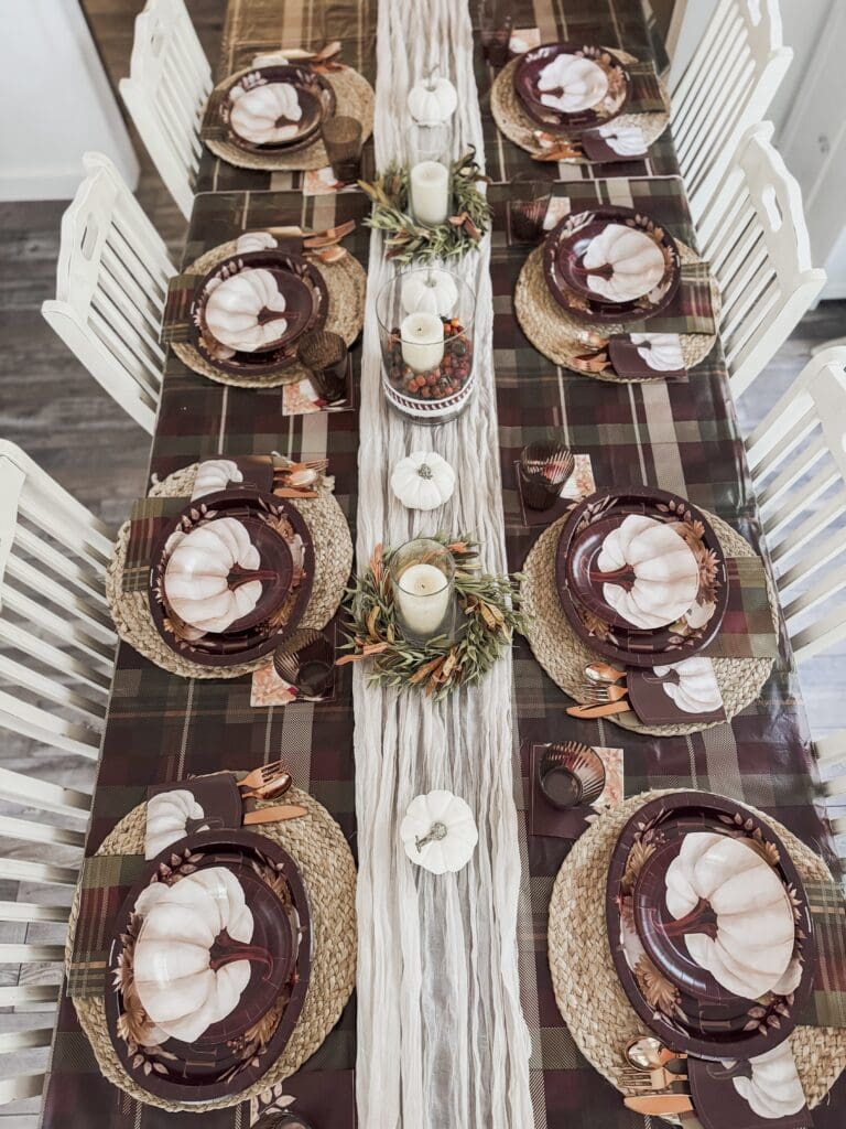 Elegant fall-themed dining table setting with white pumpkins, candles, and autumn accents for a cozy Thanksgiving dinner.
