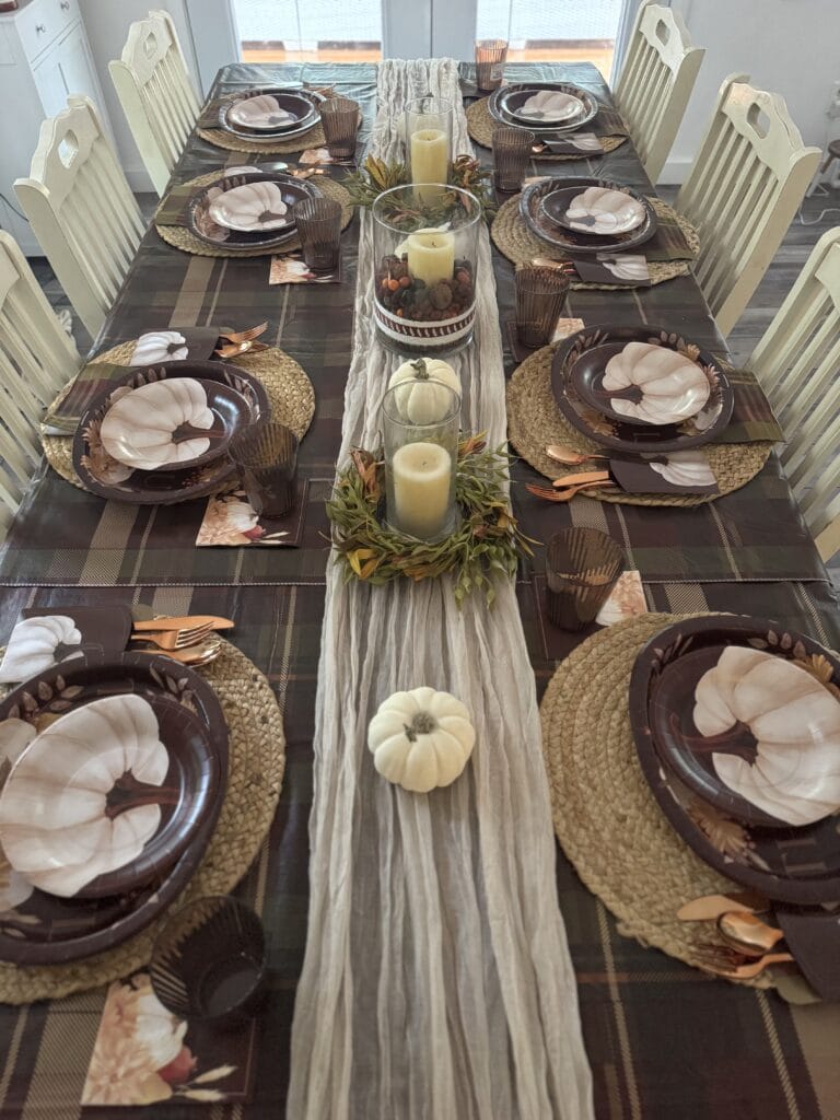 Autumn-themed dining table setup with pumpkin plates, fall foliage, candles, and woven placemats for a cozy harvest celebration.