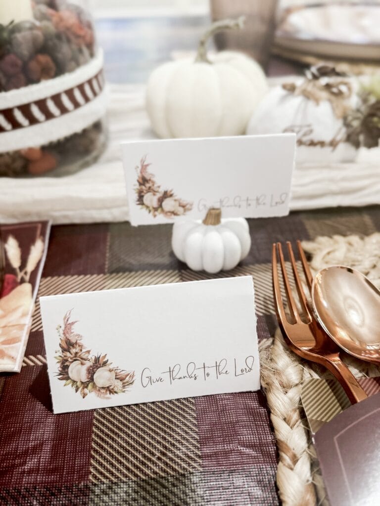 Soft white pumpkins and autumn-themed place cards with floral accents, perfect for fall gatherings and Thanksgiving table decor.