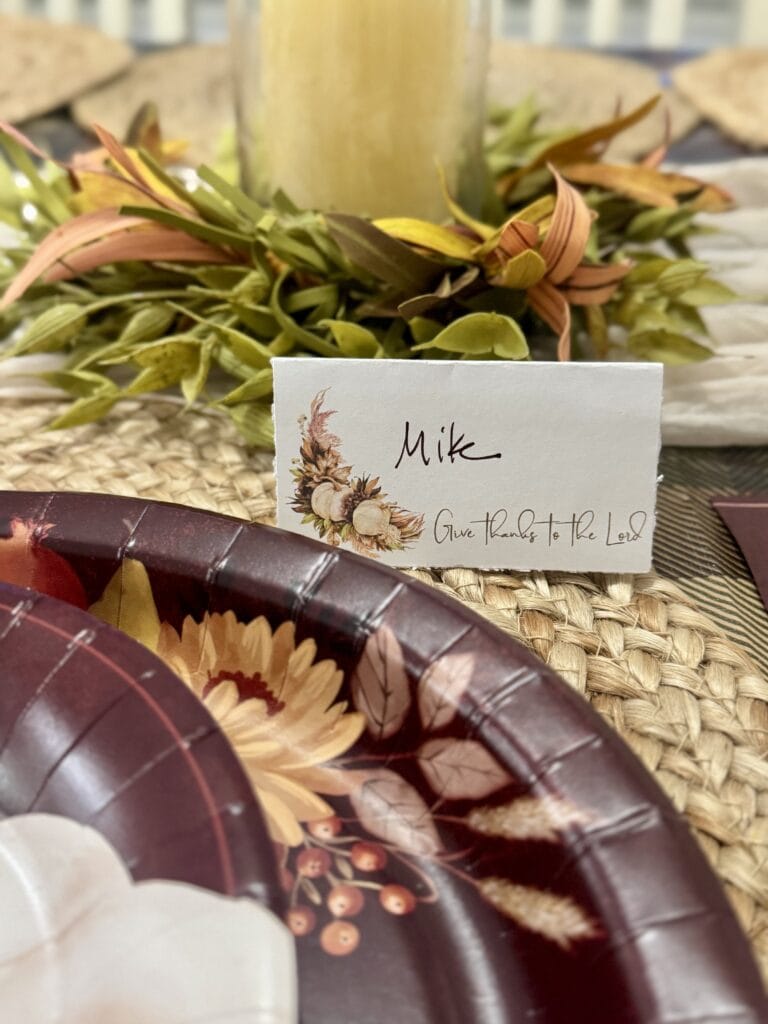 Autumn centerpiece with a candle, dried leaves, and a personalized name card for a fall celebration or Thanksgiving table.