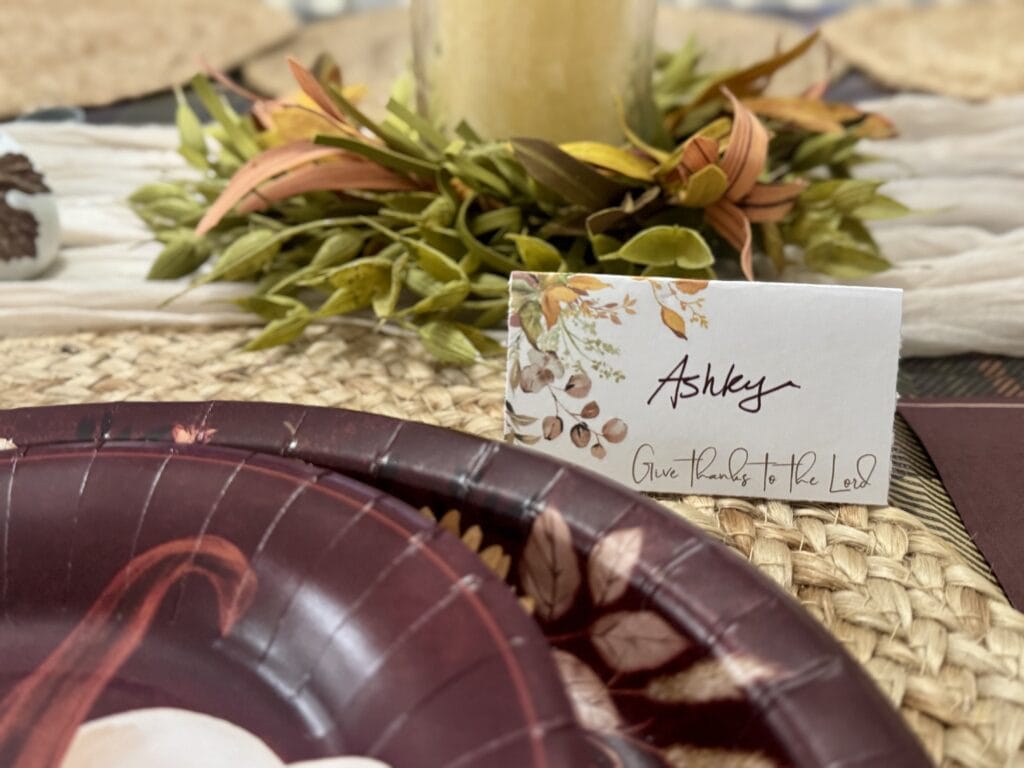 A Hundred Affections fall-themed place setting with a gratitude card, a plate with autumn leaf design, and decorative foliage for Thanksgiving or harvest celebration.