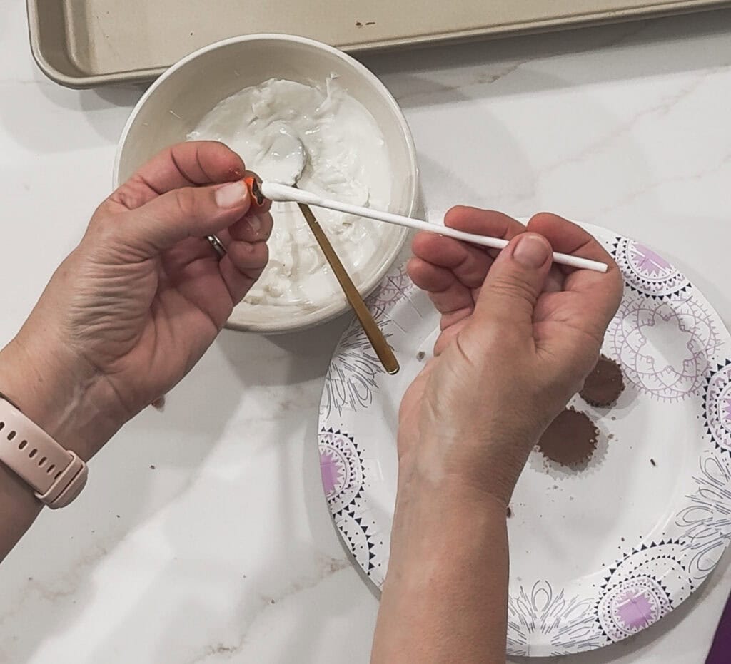 Cream white chocolate being decorated with a spoon and cake pop sticks for homemade treats.