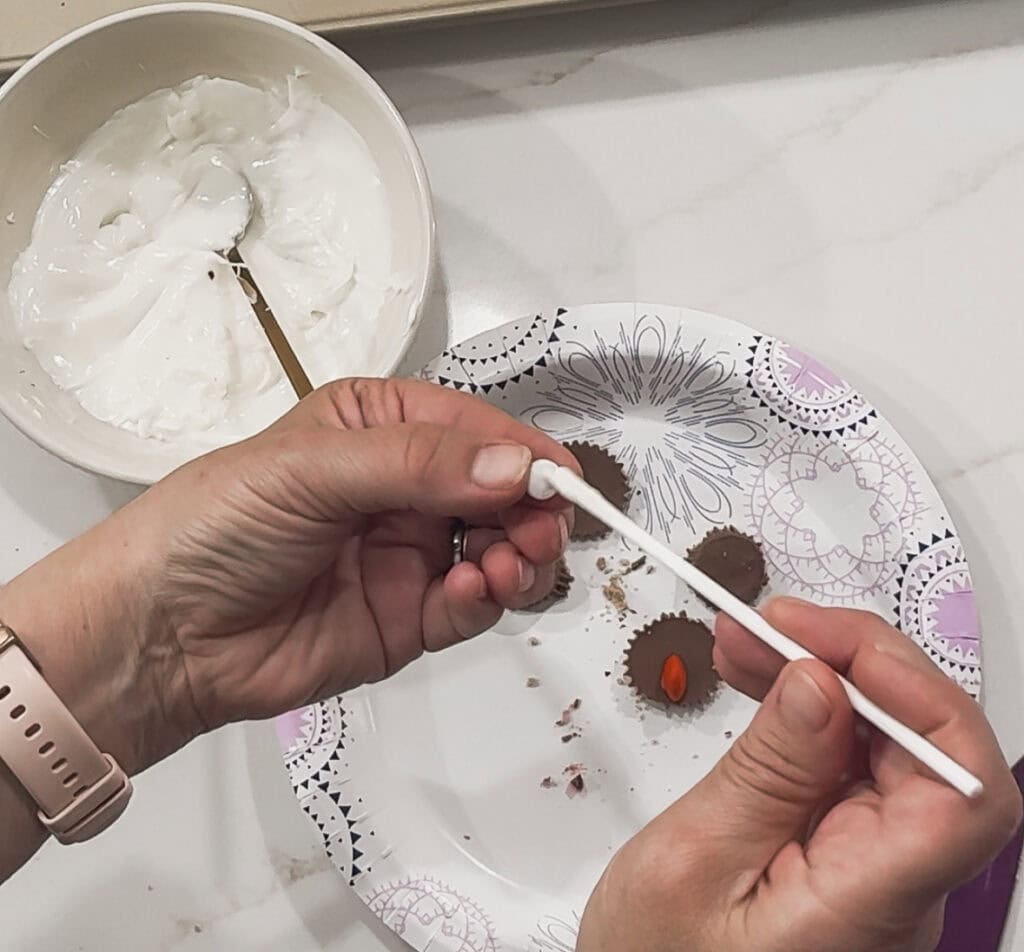 Decorating chocolates with white frosting on a festively patterned paper plate, showcasing homemade dessert making, perfect for special occasions and sweet treats.