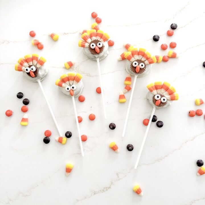 Colorful turkey cake pops with candy corn, Halloween-themed desserts, and M&M candies on a white marble background.