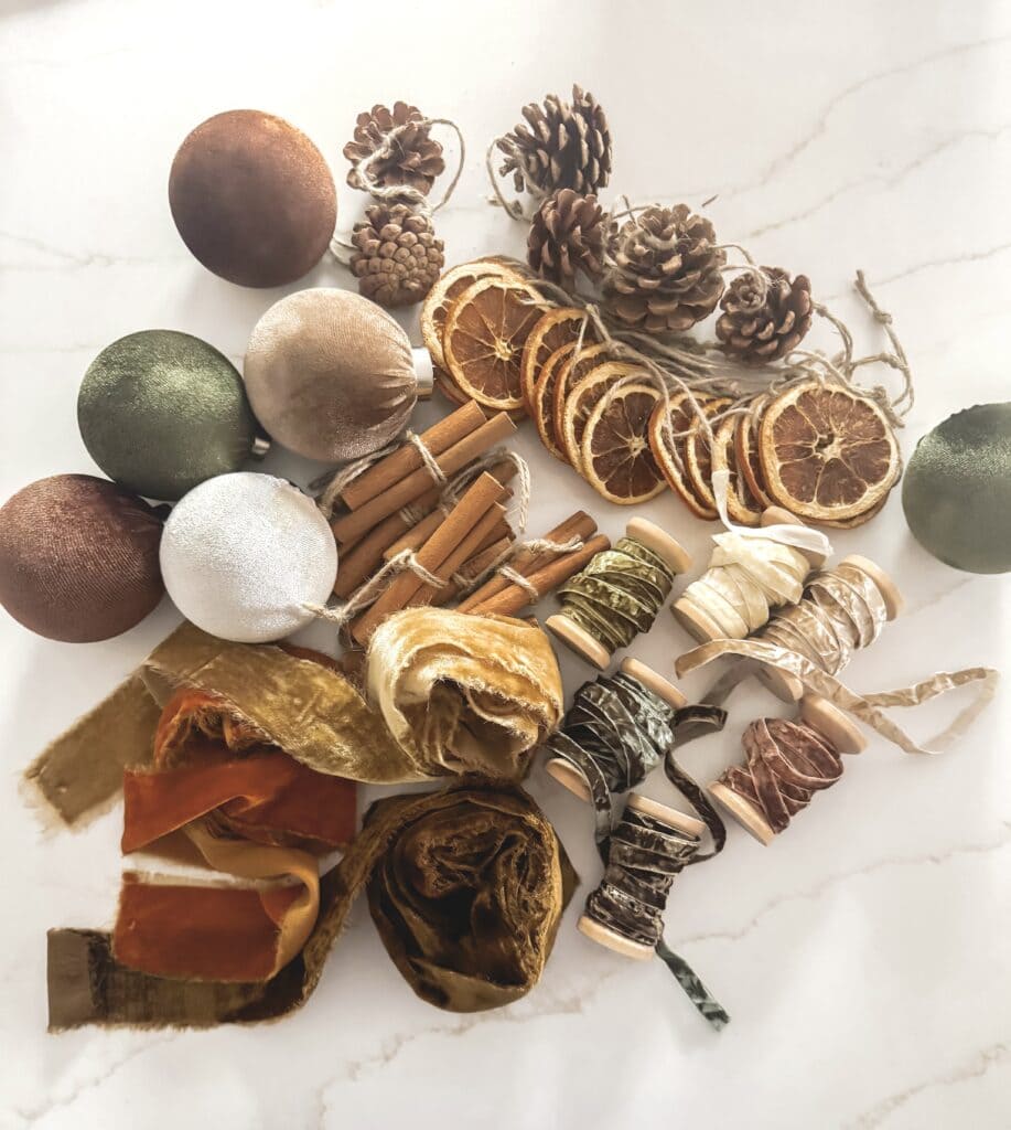 Dried orange slices, cinnamon sticks, pinecones, and decorative ornaments on a marble surface for holiday and Christmas decor.