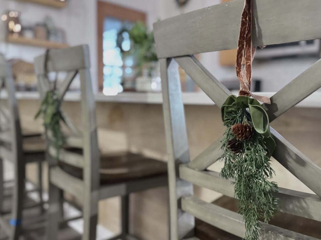 Rustic holiday decor with greenery and pinecone embellishments on wooden chair backs for festive Christmas celebrations.