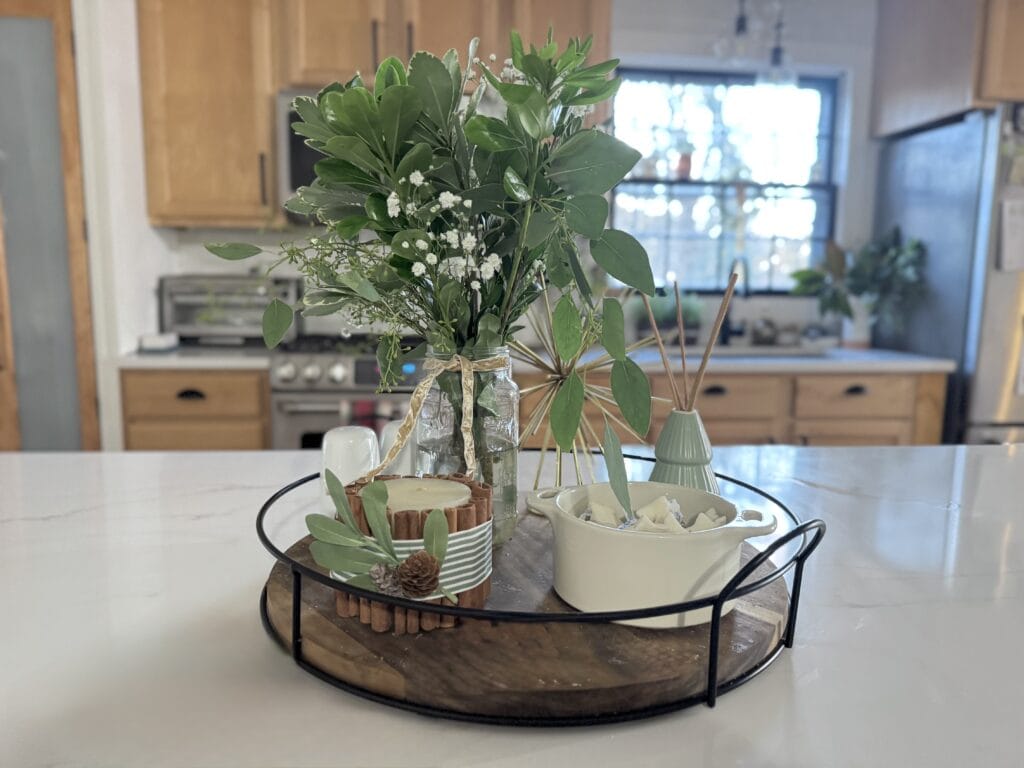 Fresh greenery centerpiece arranged on a wooden tray with candles and decorative vases for cozy, rustic home decor.