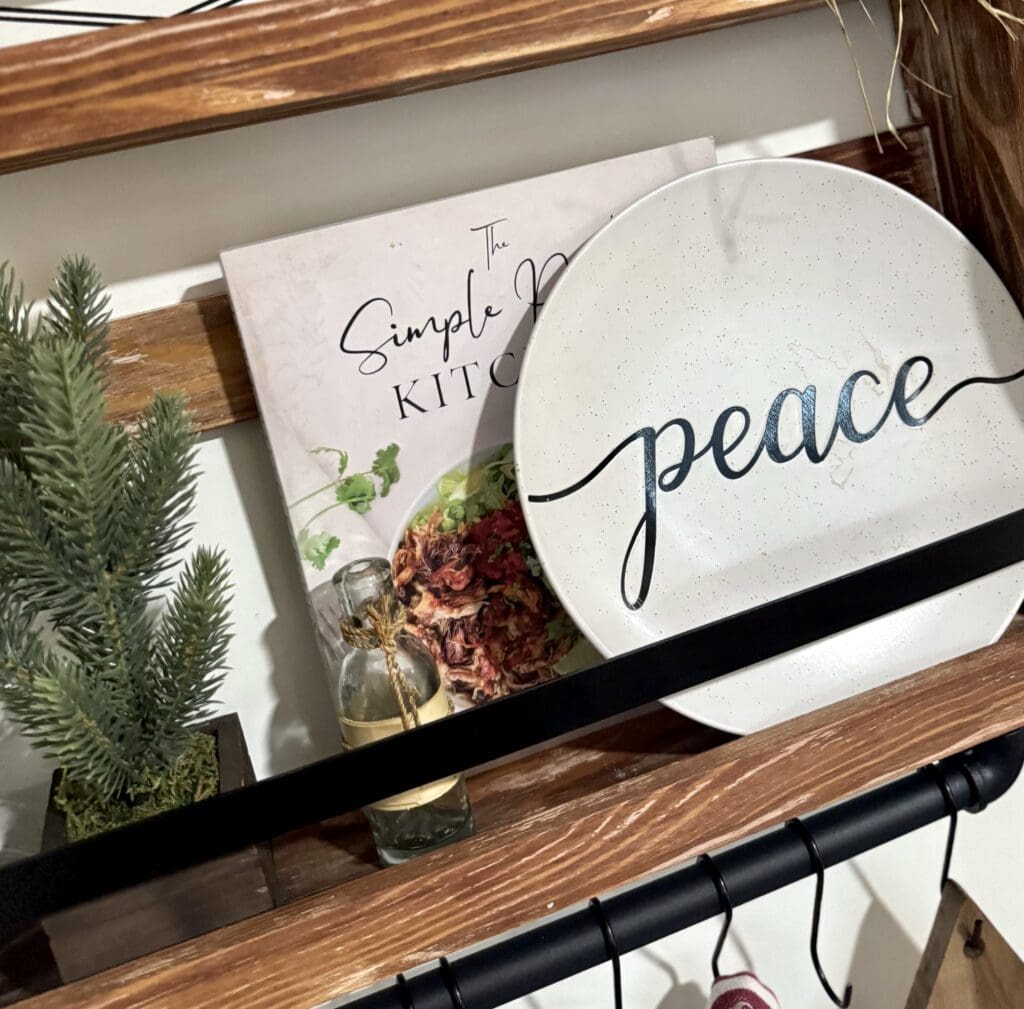 A festive wooden tray displaying a peace-themed plate and a kitchen cookbook with dried flowers and a small pine tree, perfect for holiday home decor.