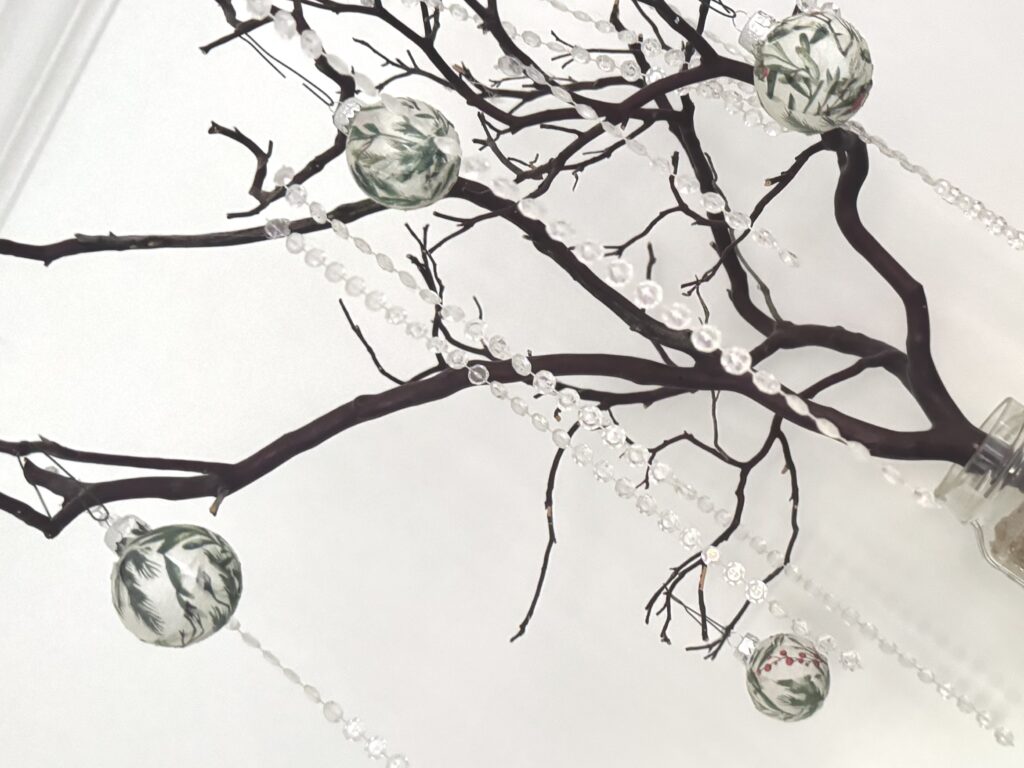 Decorated tree branch with hanging ornaments and bead garlands, elegant home decor centerpiece, stylish accent for interior spaces.