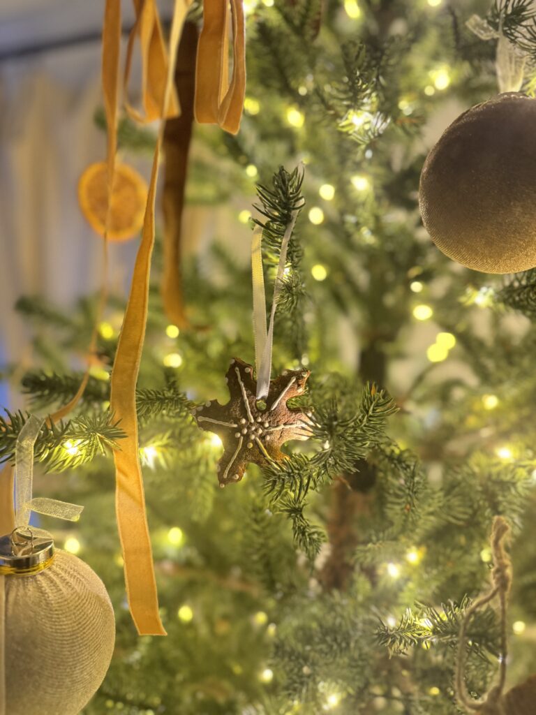 Ornament decorated Christmas tree with gold baubles, star-shaped cookie, and ribbons, illuminated by warm fairy lights, capturing festive holiday spirit and cozy winter celebration.