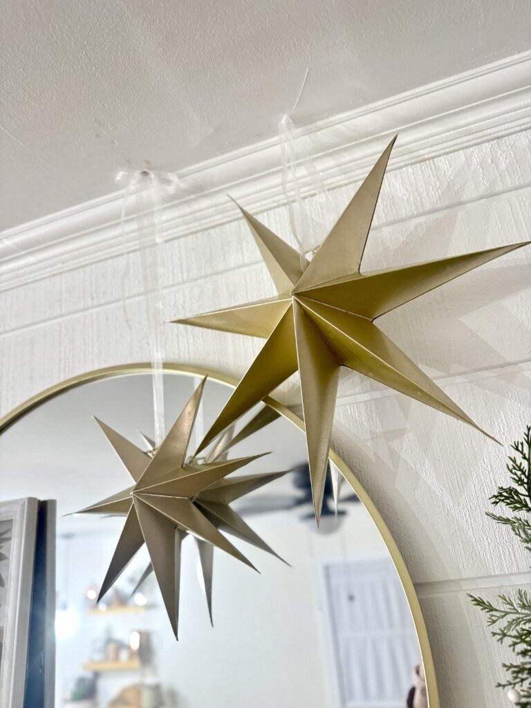 Decorative gold paper star ornaments hanging above a round mirror in a cozy, festive indoor setting.