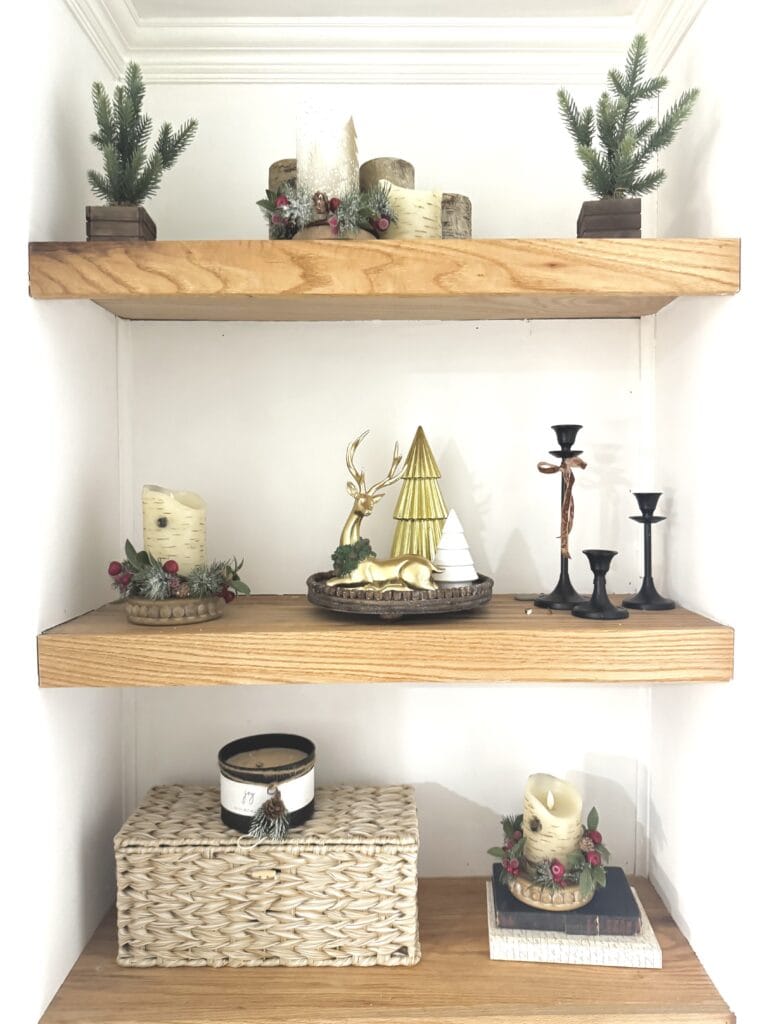 Festive holiday decoration display with candles, pine branches, and holiday-themed accents on wooden shelves.
