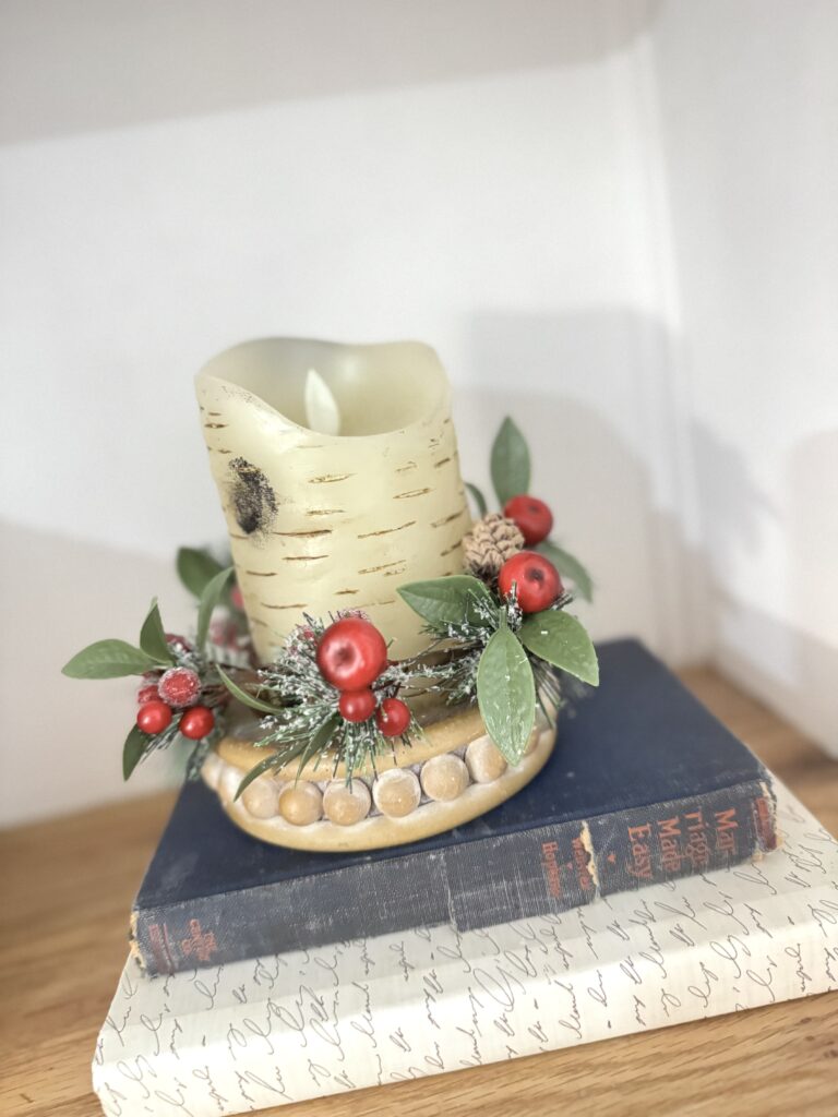 Vintage candle holder with Christmas greenery and red berries on top of a closed antique book, holiday decor, cozy festive atmosphere.