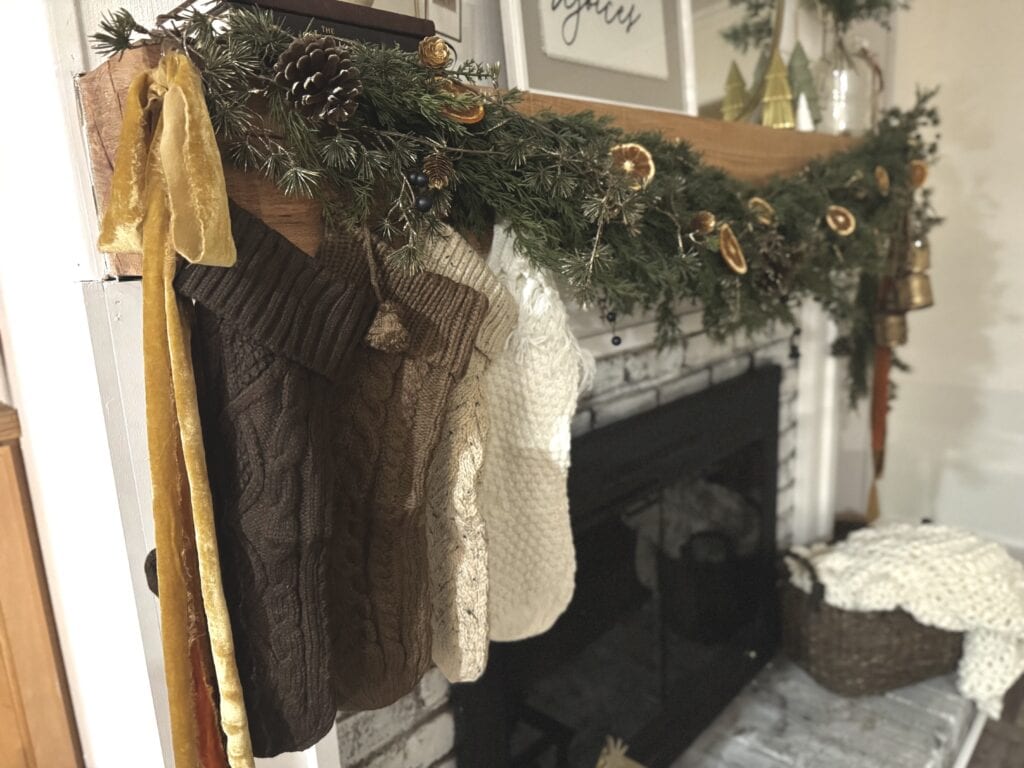 Cozy Christmas stockings hanging on a fireplace decorated with festive greenery, pinecones, dried orange slices, and gold accents, perfect for holiday home decor.