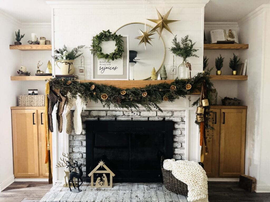Festive Christmas mantel decorated with greenery, dried orange slices, stockings, and rustic accents in a cozy holiday living room.