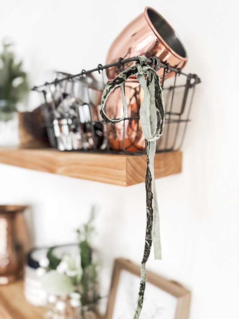 Elegant rose gold mug resting on a black wire basket with a patterned headband draped over the edge, showcasing trendy home decor and accessories.