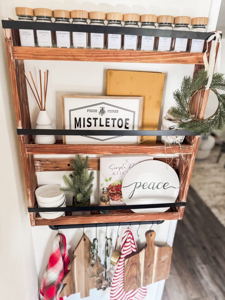 Spice jar shelf with herbs and kitchen decor, wooden spice jars, holiday wreath, and vintage inspired kitchen signs, cozy rustic home decor.