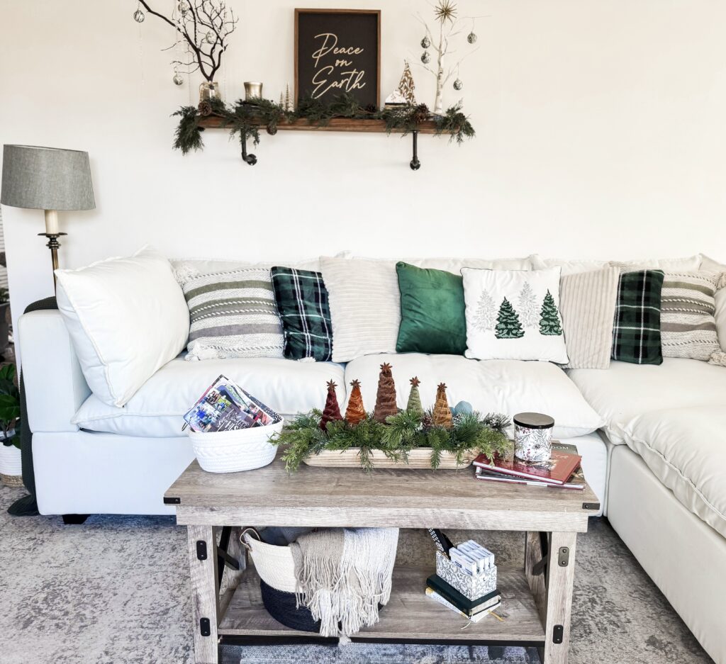 Festive Christmas living room decor with holiday-themed pillows, pinecone accents, greenery, and a "Peace on Earth" sign for cozy holiday home inspiration.