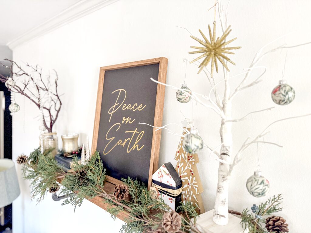 Festive holiday decor with a white-painted tree, ornaments, pinecones, and greenery, featuring a blackboard sign with "Peace on Earth" in elegant script, perfect for Christmas celebrations.