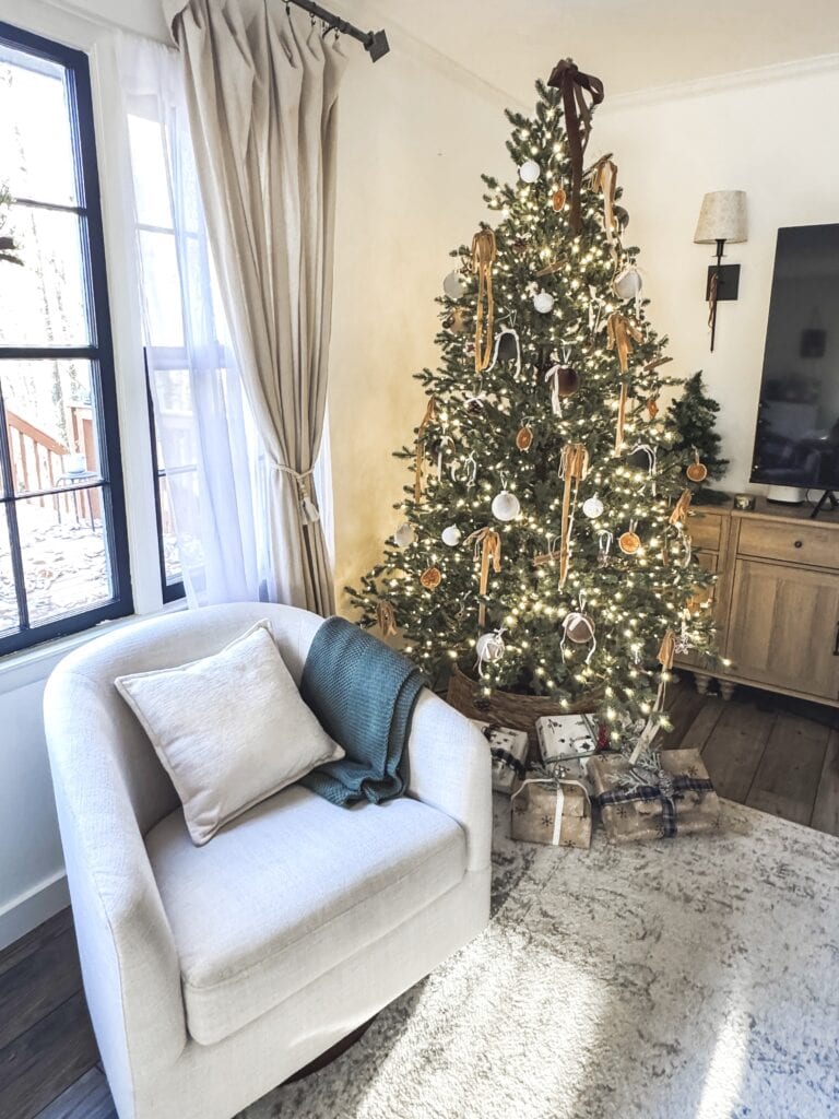 Festive decorated Christmas tree with ornaments and lights in a cozy living room.