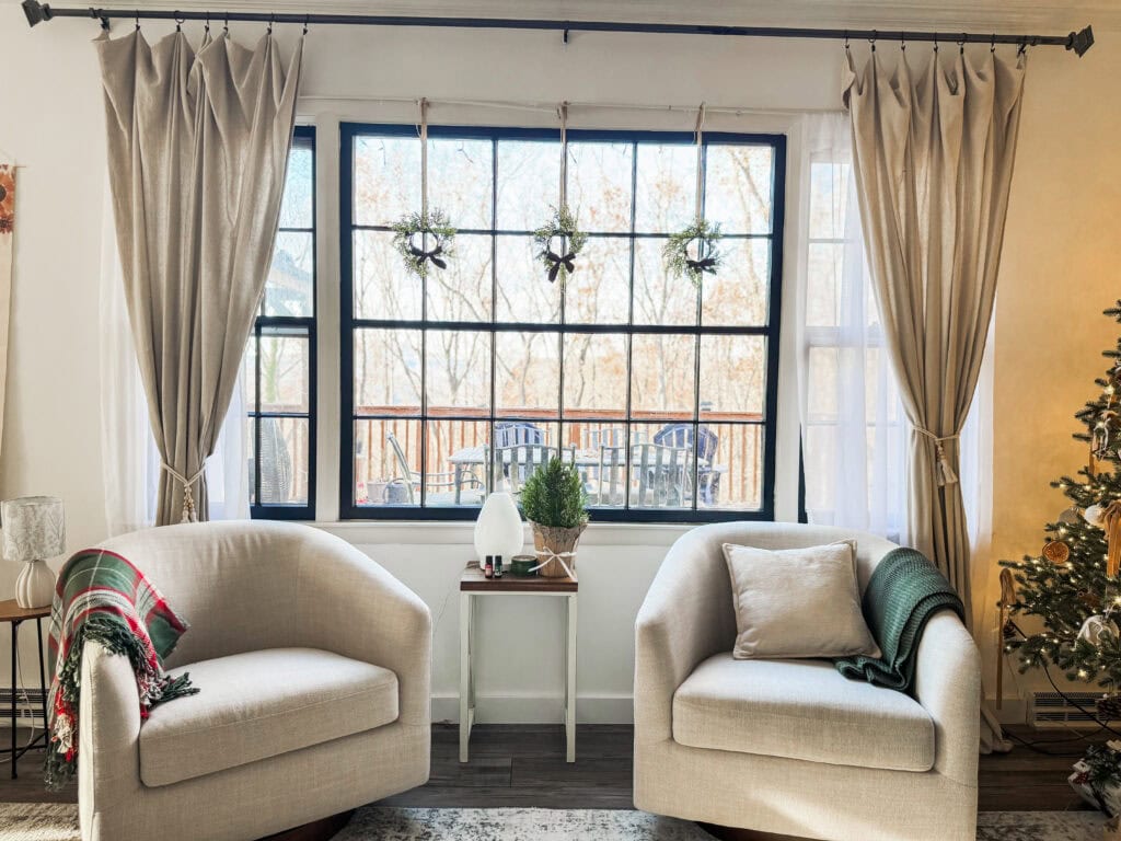 Cozy living room decor with large window, beige armchairs, holiday decorations, and Christmas tree for festive home interior.