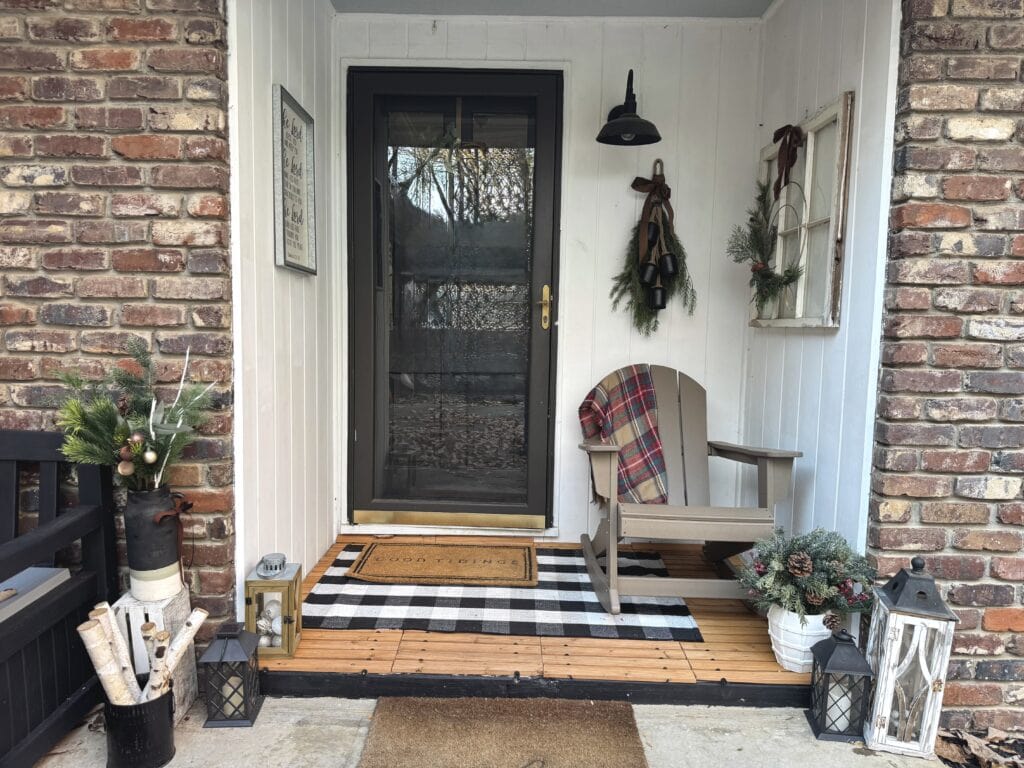 Cozy holiday porch decorated with evergreen accents, lanterns, and a plaid blanket draped over an Adirondack chair, creating a warm and inviting entrance in winter.
