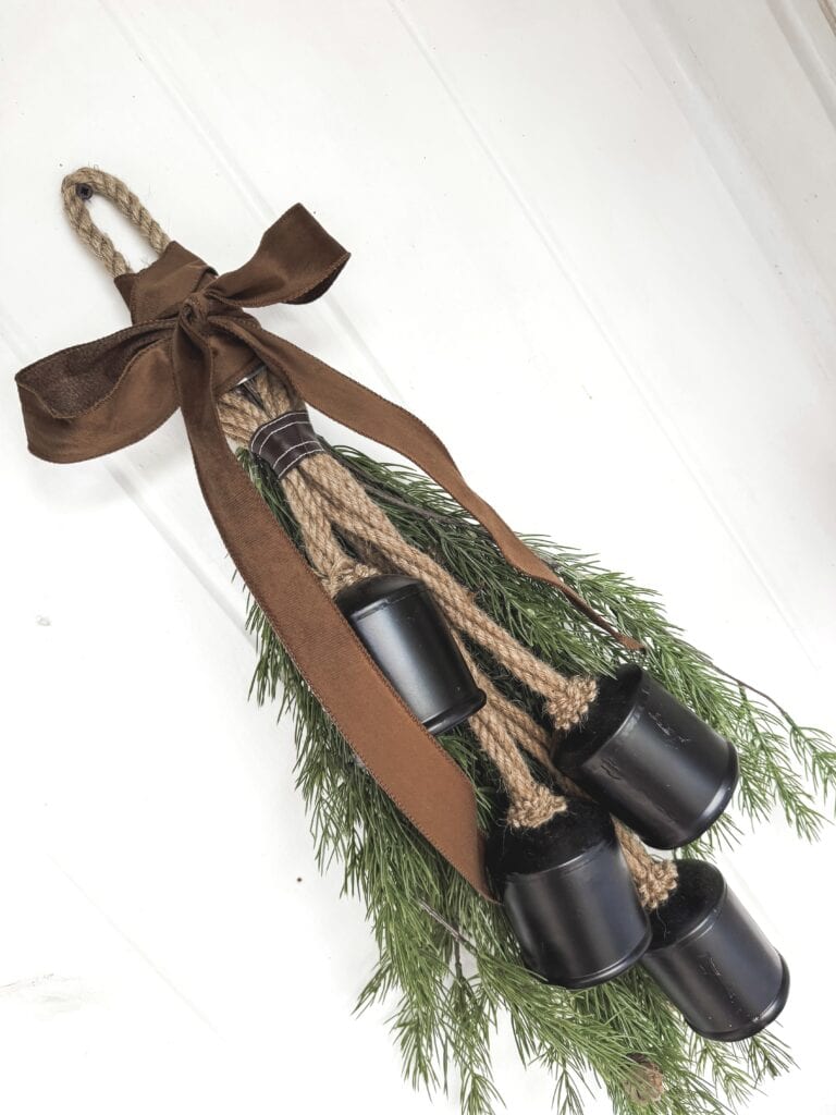 Rustic Christmas door hanger with black bells, evergreen sprigs, and a brown ribbon bow for holiday decor.