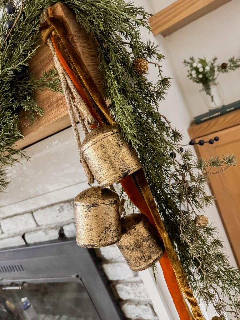 Vintage gold jingle bells hanging from a rustic holiday garland with pine needles and small pinecones, perfect for Christmas decor enhancement.