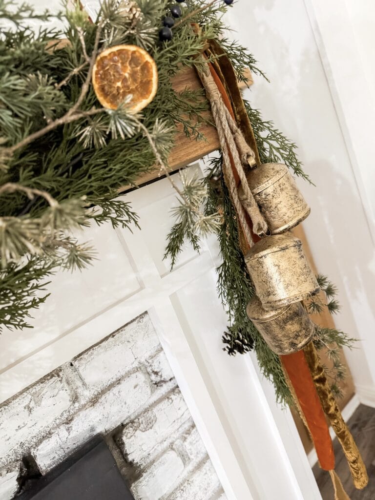 Dried orange slices and evergreen garland decorating a rustic fireplace mantel for Christmas.