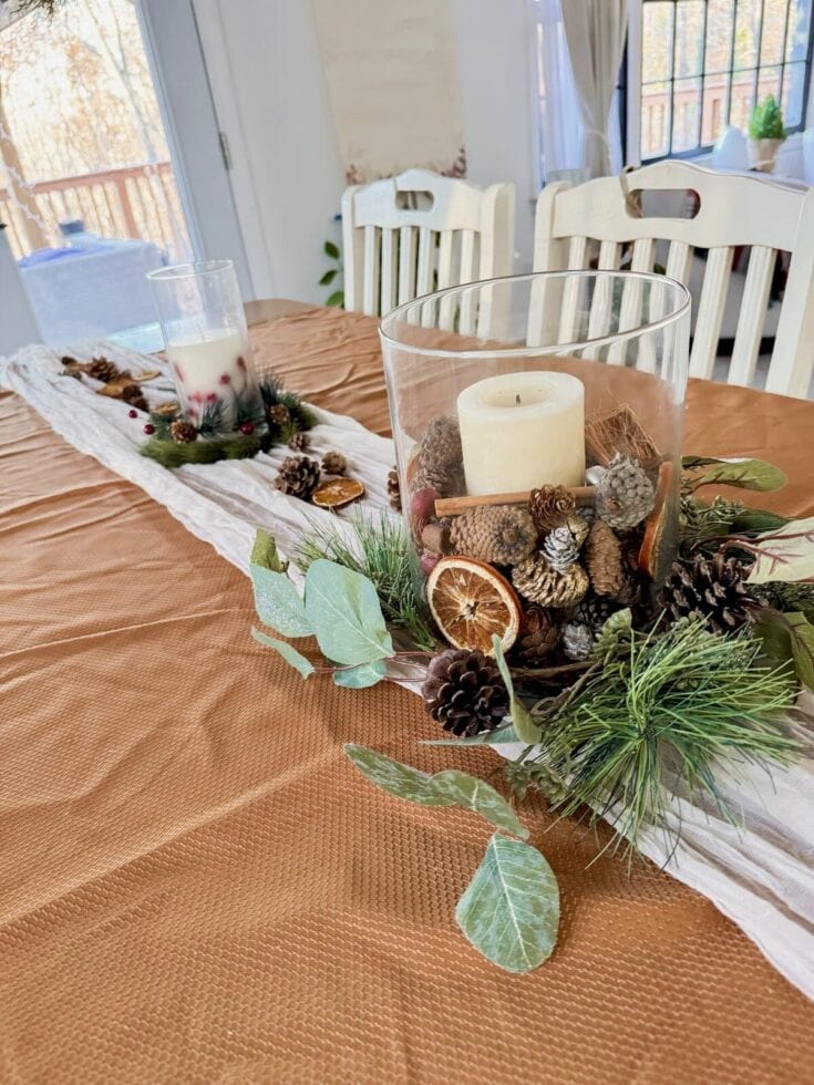 Festive holiday table centerpiece with candles, pinecones, dried citrus slices, and greenery for Christmas or winter decor.
