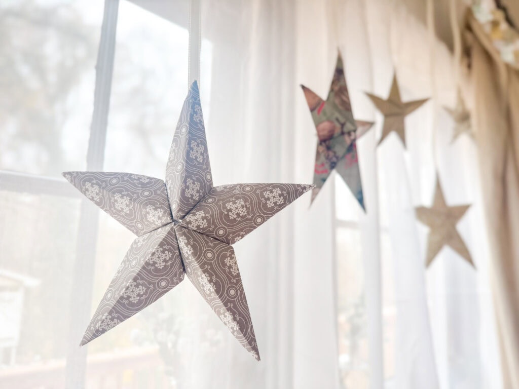 Decorative paper star Christmas ornaments hanging indoors with natural light, holiday home decor, Christmas decorations, and warm seasonal ambiance.