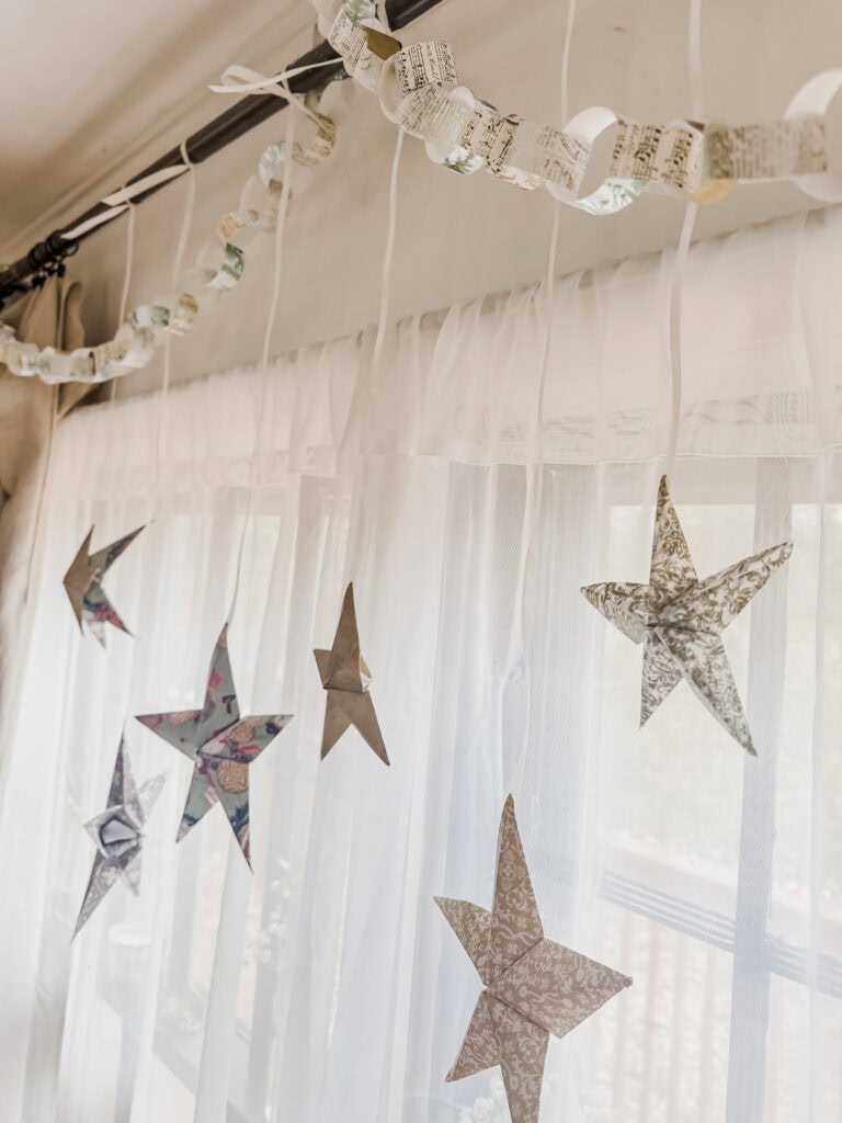 Decorative paper stars hanging from a curtain rod with sheer curtains, creating a whimsical and cozy home decor aesthetic.