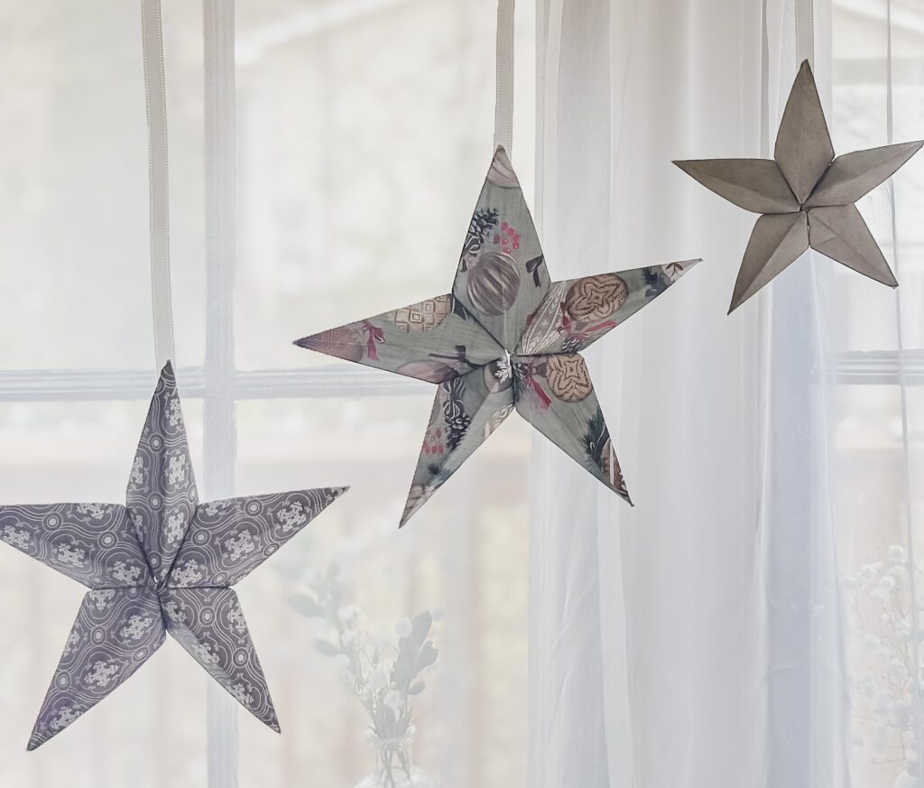 Colorful paper star ornaments hanging by a window for festive holiday decor, creating a cozy and charming atmosphere.