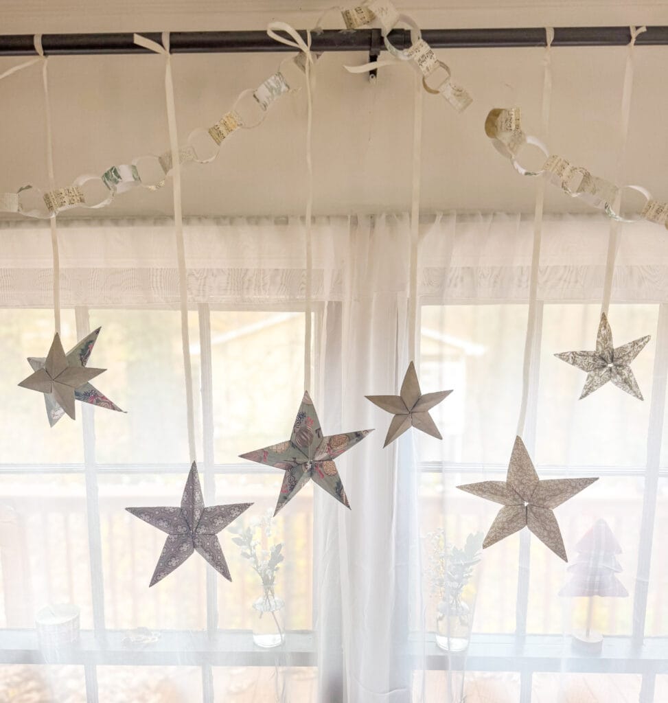 Colorful origami star and moon decorations hanging in front of a window with sheer curtains, creating a cozy and festive atmosphere for holiday or special occasion celebrations.