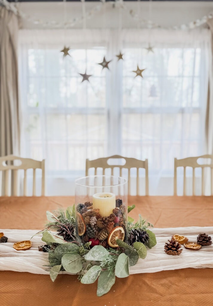 Layered centerpiece with pinecones, dried citrus slices, and greenery on a rust-colored tablecloth, ideal for festive holiday or winter celebrations.